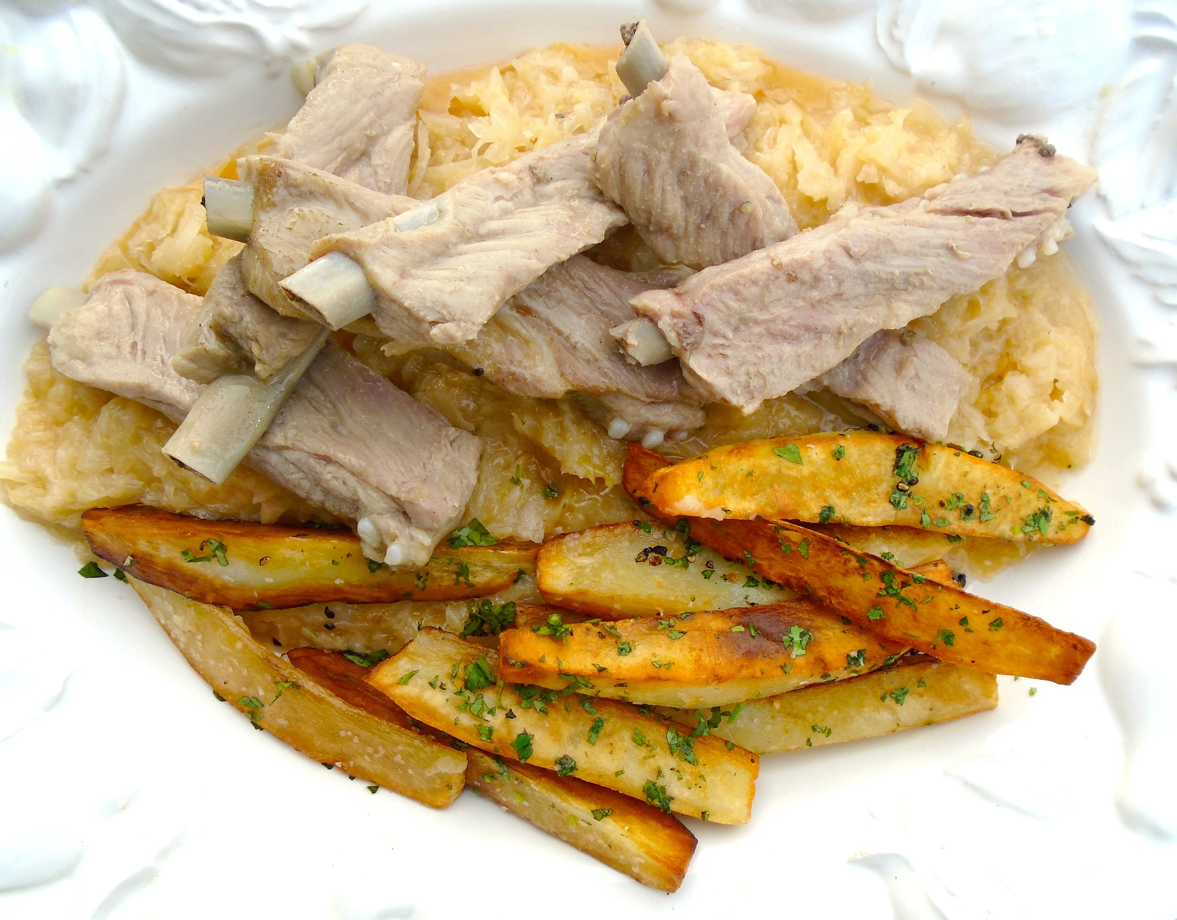 Die fertig gegarten Schälrippchen auf dem Sauerkraut und den Bratkartoffeln anrichten