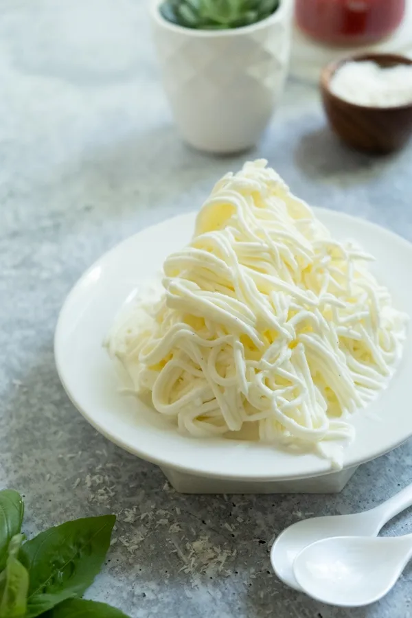 Die frisch gepressten Vanilleeis-Spaghetti liegen auf der Schlagsahne auf einem Teller