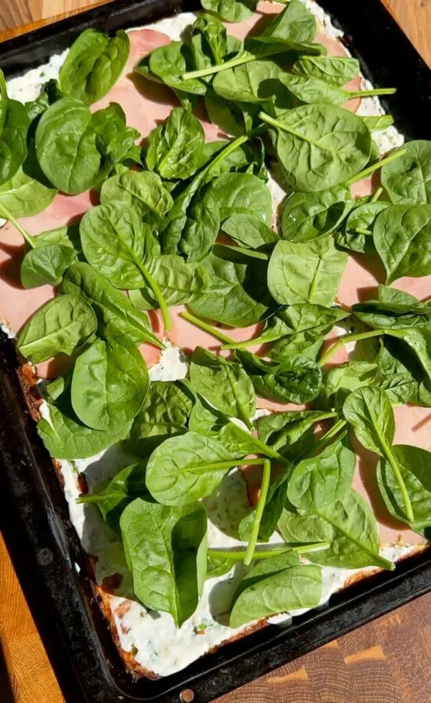 Die Frischkäsefüllung wird auf dem Low Carb Gemüse-Boden verstrichen, belegt mit Schinken und frischem Spinat