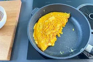 Die goldbraune Omeletthälfte wird gekonnt umgeschlagen und auf einen Teller gleiten gelassen, fertig zum Servieren.