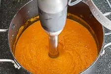 Die Karotten Ingwer Suppe wird mit einem Pürierstab cremig gemixt, bevor sie abgeschmeckt und serviert wird.