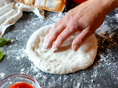Die Zubereitung eines glutenfreien Pizzateigs, der sorgfältig geformt wird.