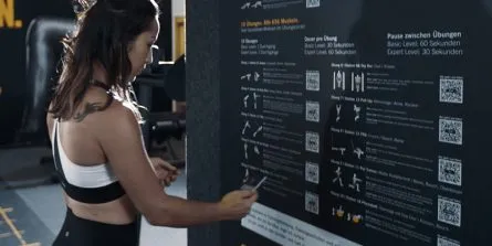 Digitale Trainingsunterstützung mittels QR-Codes und interaktiven Touchscreens im Frauen-Fitnessstudio.