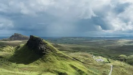 Dramatische Landschaft der Isle of Skye in Schottland, mit üppigen grünen Wiesen, zerklüfteten Bergen und einem dunklen Himmel.