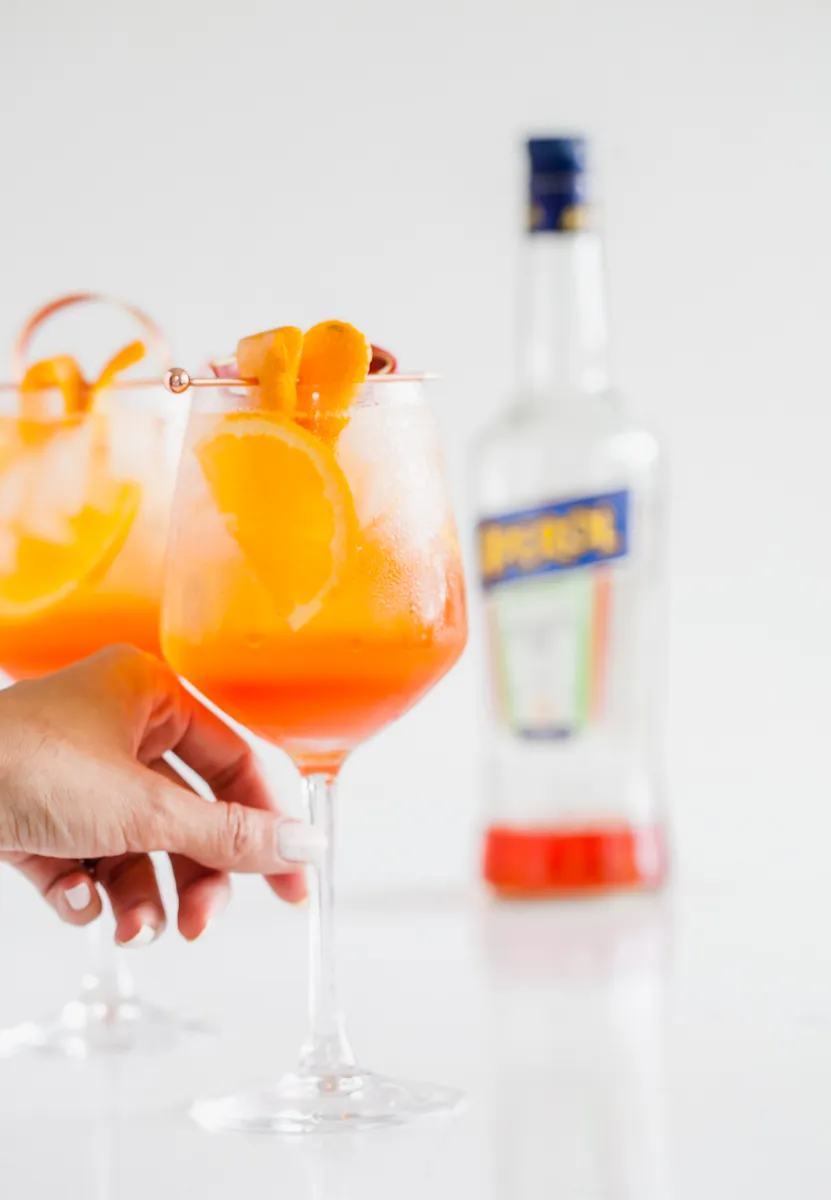 Draufsicht auf drei Rhabarber Aperol Spritz mit Eis, Rhabarberdeko und Orangenscheiben auf einem Tisch.