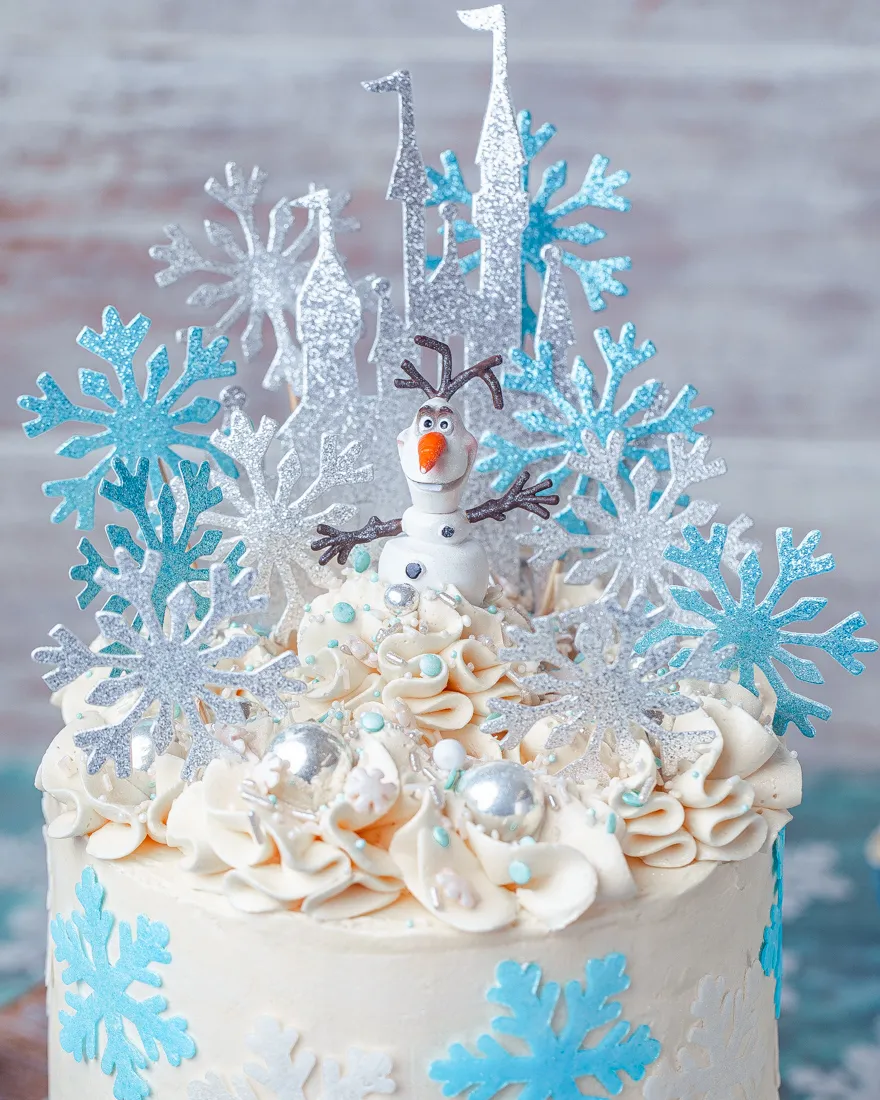 Drei Elsa Figuren auf einer Frozen Torte, mit blauen Zuckerperlen und weißen Schneeflocken