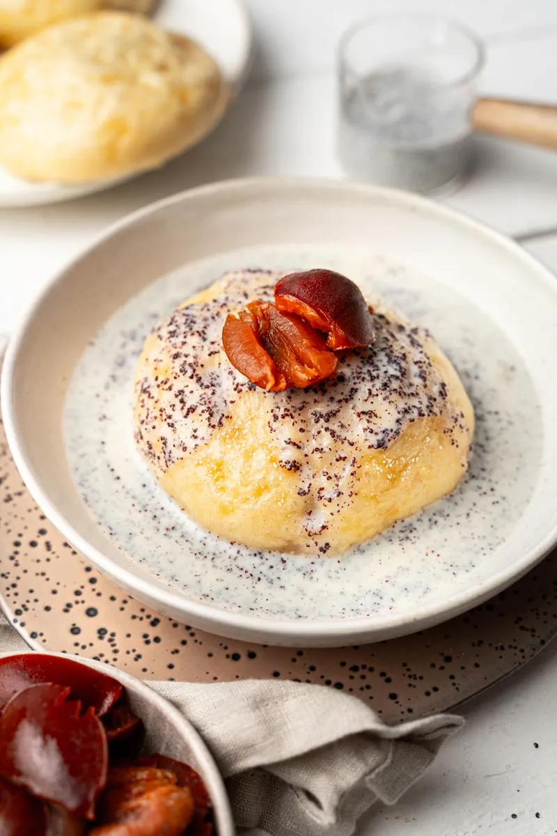 Drei Germknödel mit goldbraunem Hefeteig und üppiger Vanille-Mohn-Soße, bereit für den Familien-Esstisch.