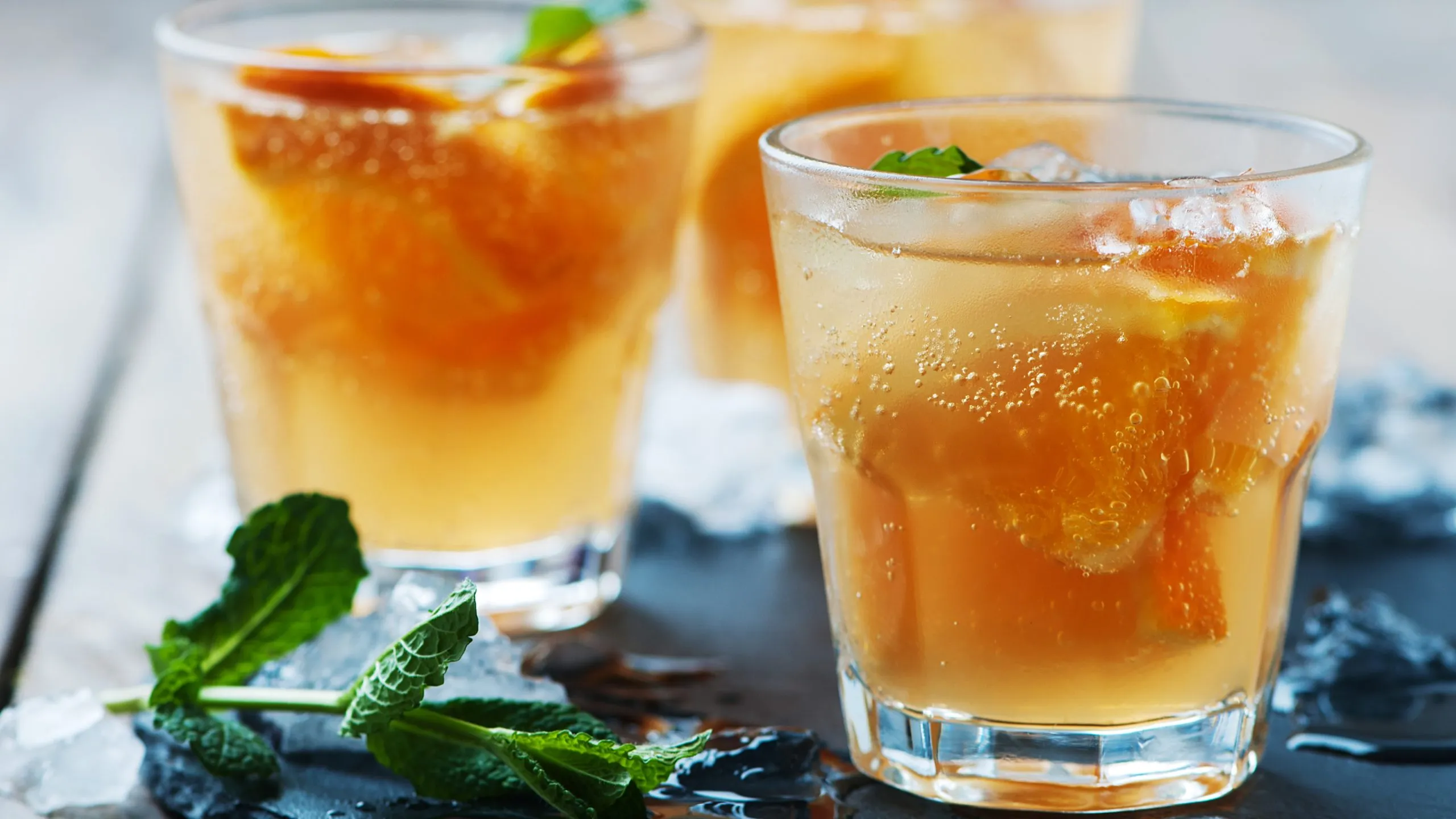 Drei Gläser Lillet Orange Spritz auf Holztisch mit Minze und Orangen