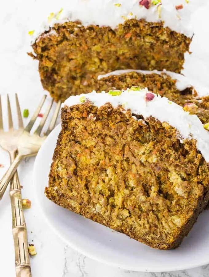 Drei saftige Scheiben veganer Karottenkuchen, serviert auf einem weißen Teller.