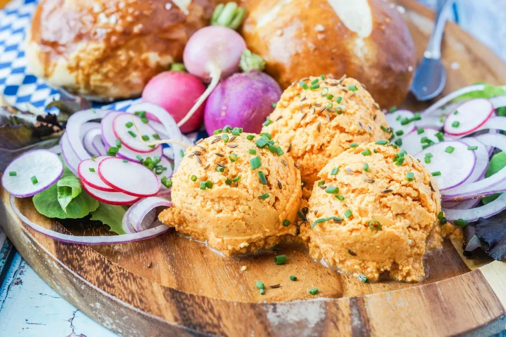 Drei Schalen Obazda (bayerischer Käse- und Bier-Dip) auf einem Holzbrett.