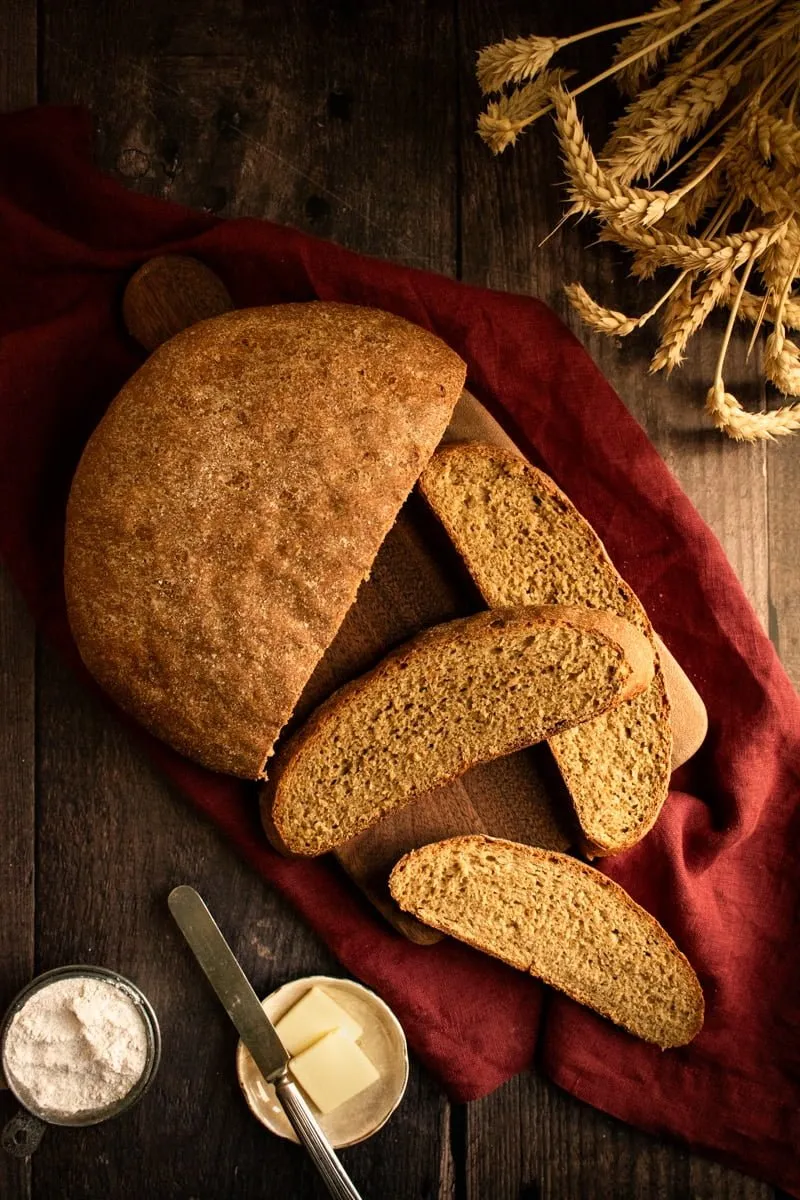 Drei Scheiben Roggenbrot auf einem Holzschneidebrett neben dem restlichen Laib.