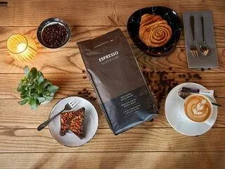 Dunkel geröstete Espresso Superior Kaffeebohnen, bereit für den Kaffeevollautomaten, zusammen mit einem Gebäck