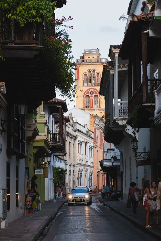 Dunkle Gasse gesäumt von historischen bunten Häusern, im Hintergrund ein gelb-oranger Turm