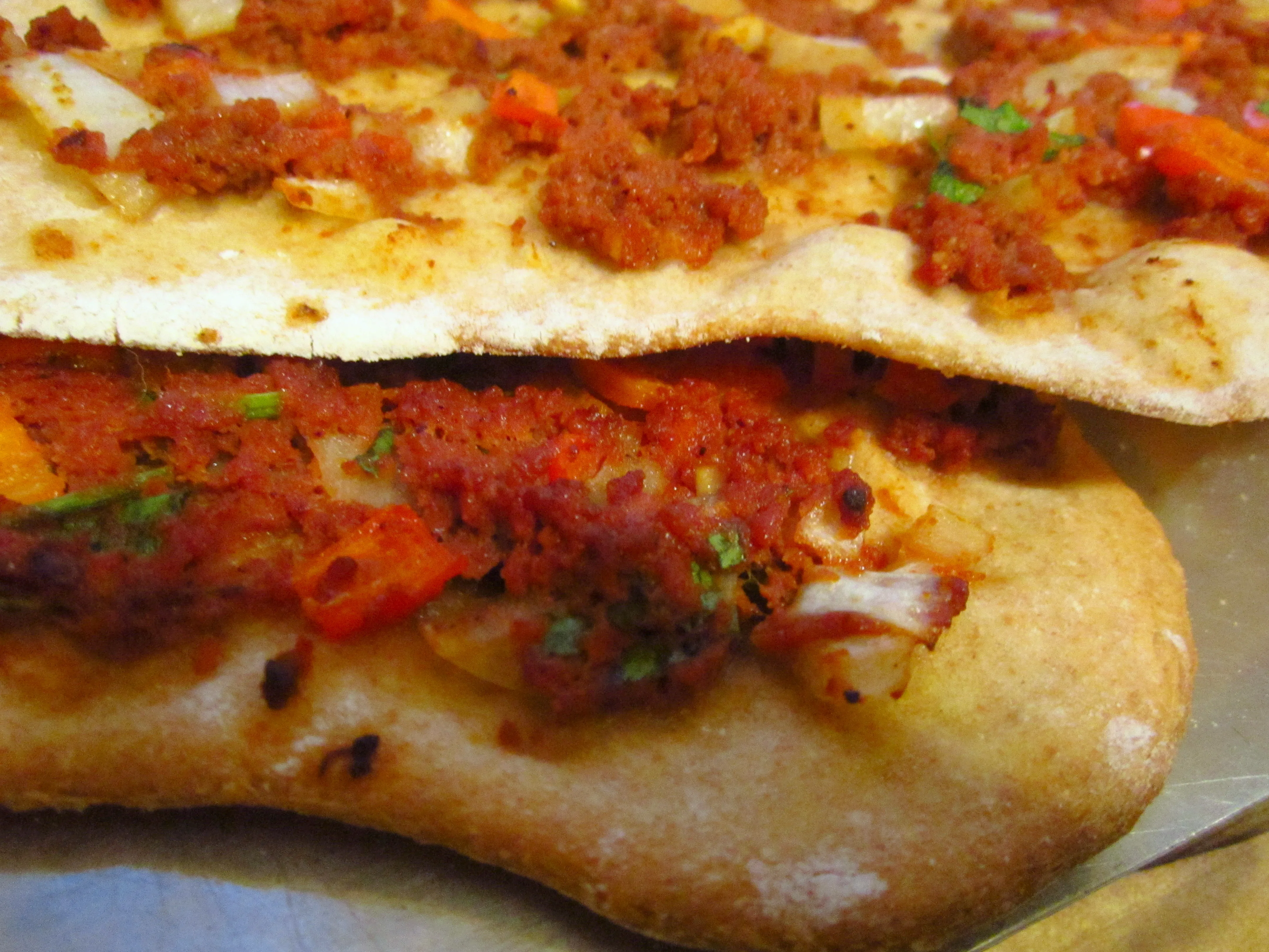 Dünn ausgerollter Lahmacun-Teig, reichlich belegt mit einer würzigen Hackfleisch-Paprika-Paste, bereit zum Backen.