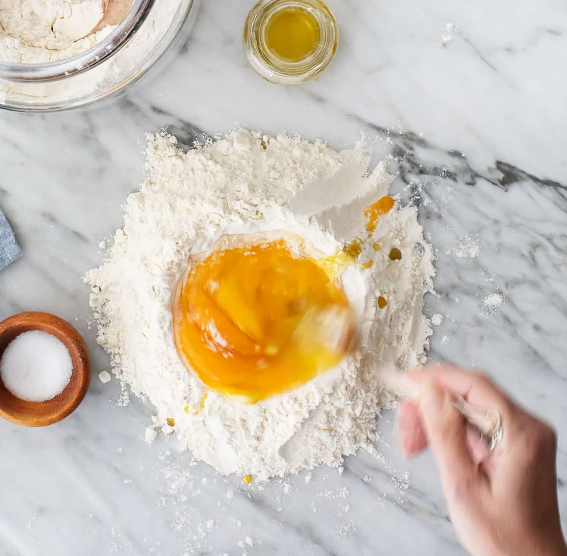 Eier werden vorsichtig mit einer Gabel in einem Mehlkreis auf der Arbeitsfläche verquirlt, um den Nudelteig für Linguine vorzubereiten.