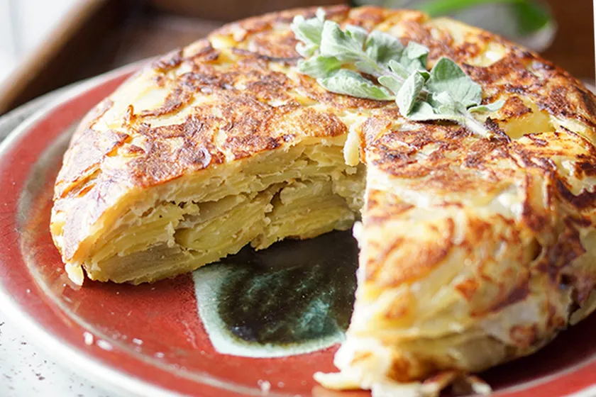 Ein appetitliches Stück goldbraune Spanische Tortilla auf einem Holzbrett, perfekt zum Servieren.