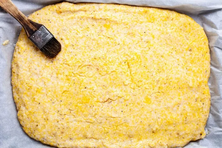Ein Backpinsel liegt auf einem Polenta Pizza Boden, der mit Olivenöl bestrichen wurde, vor dem Vorbacken.