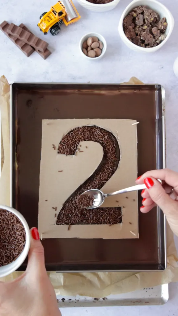 Ein Bagger-Geburtstagskuchen wird mit Schokolade und Baustellenfahrzeugen dekoriert