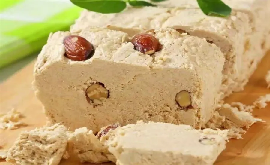 Ein Block Halawa, eine Süßigkeit aus Sesampaste, mit Pistazien garniert, auf einem Holztisch