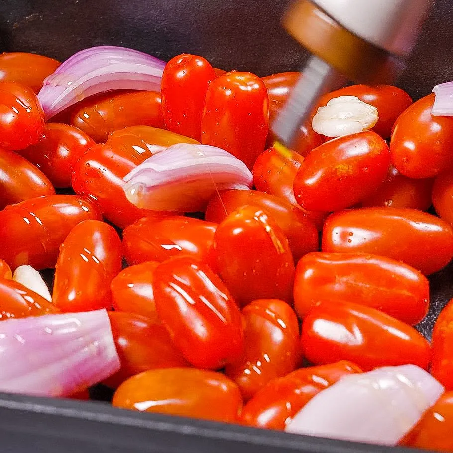 Ein Block Schafskäse wird auf Kirschtomaten, Schalotten und Knoblauch in einer Auflaufform platziert, mit Olivenöl und Kräutern beträufelt, bereit zum Backen für die One Pot Pasta.