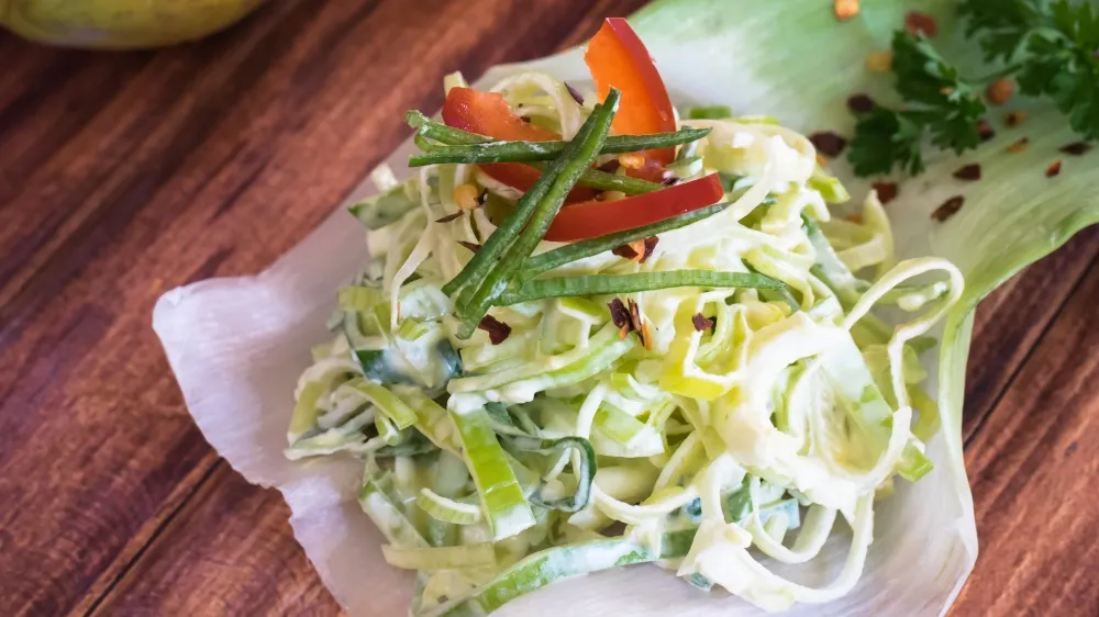 Ein bunter Papaya-Lauch-Salat mit frischen Kräutern in einer weißen Schale.