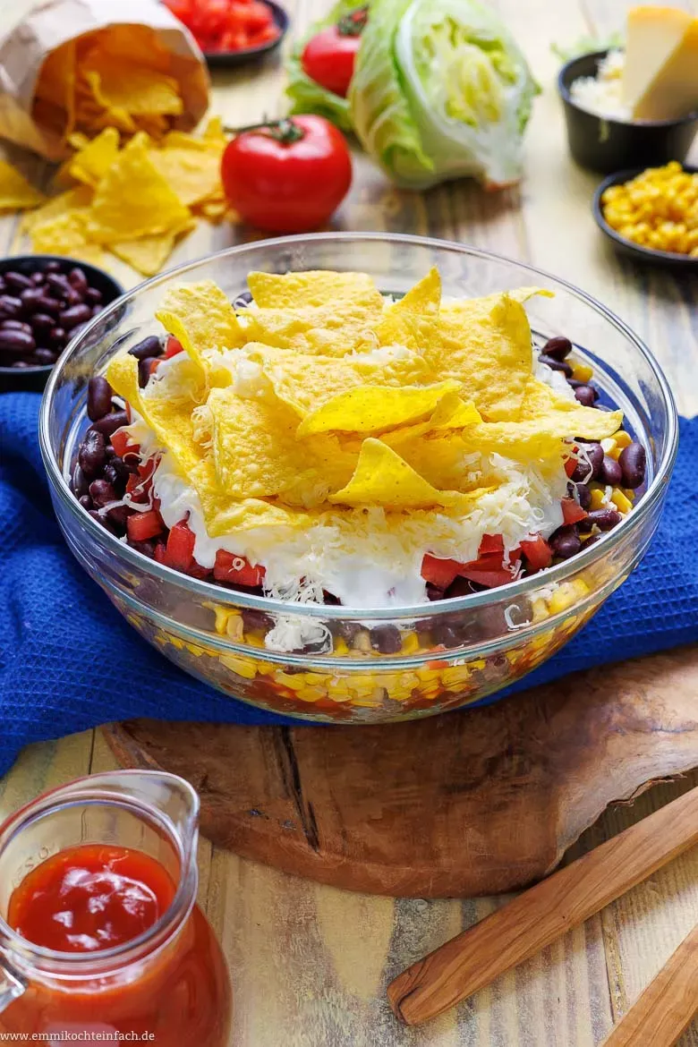 Ein bunter und appetitlicher Taco Salat mit knusprigen Tortilla-Chips, geschichtet in einer Glasschüssel, bereit zum Servieren.