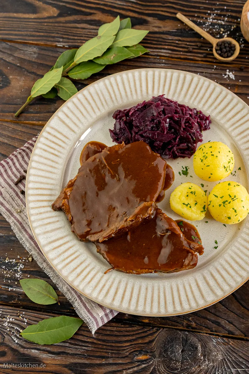 Ein butterzarter Rinderschmorbraten mit Rotkohl und Kartoffelklößen auf einem Teller.