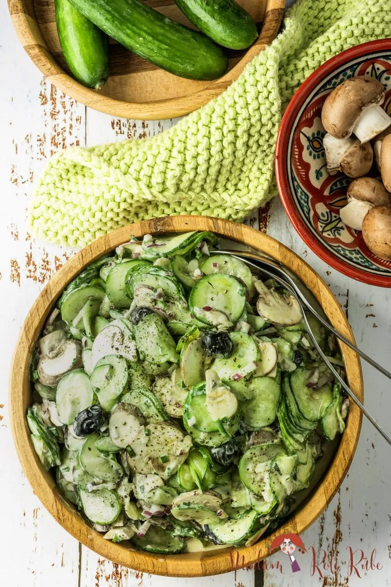 Ein cremiger Gurken-Champignon-Salat mit einem Honig-Senf-Dressing in einer Glasschüssel, dekoriert mit frischen Kräutern.