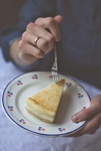 Ein cremiger New York Cheesecake von Junior's mit einer glatten, goldbraunen Oberfläche, auf einem weißen Teller mit Gabel. Perfekt für das ultimative Käsekuchen-Rezept.
