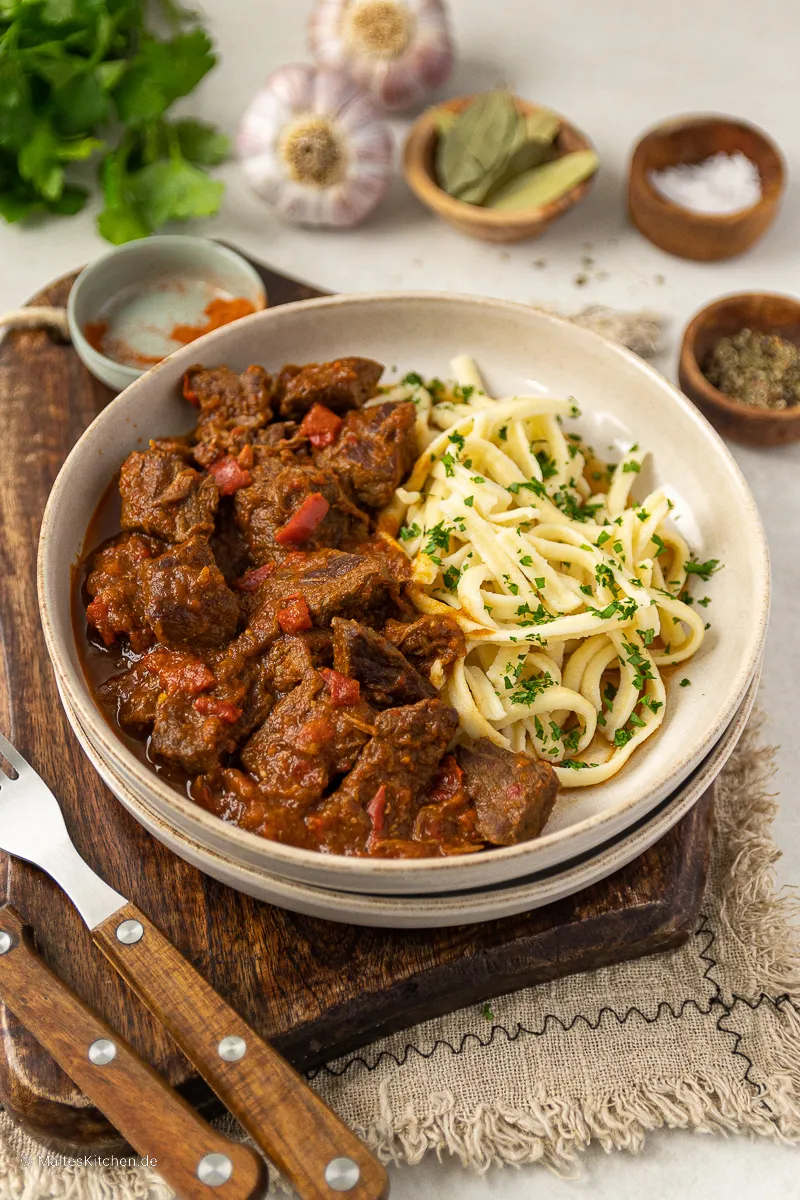 Ein dampfendes ungarisches Gulasch in einer tiefroten Sauce, garniert mit frischer Petersilie, bereit zum Servieren.
