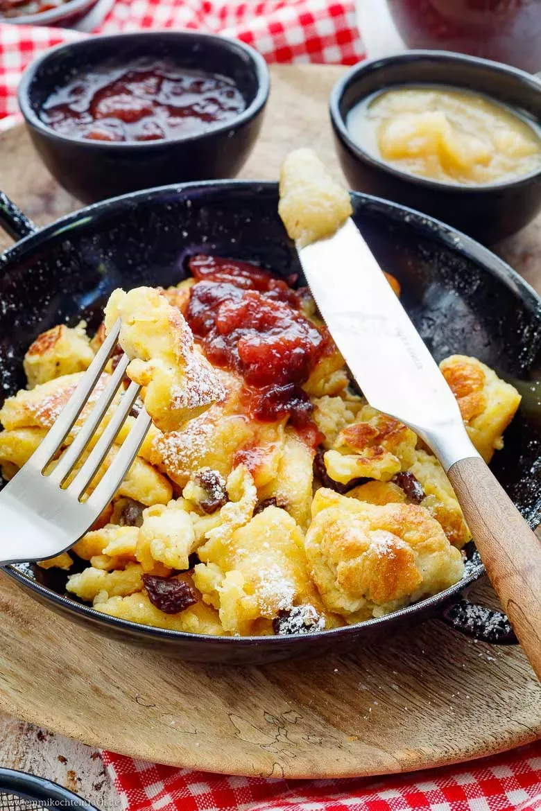 Ein detailreiches Bild von fertig zerrissenem Kaiserschmarrn, der warm und köstlich aussieht, bestäubt mit Puderzucker. Traditionelles Kaiserschmarrn Rezept für die ganze Familie.