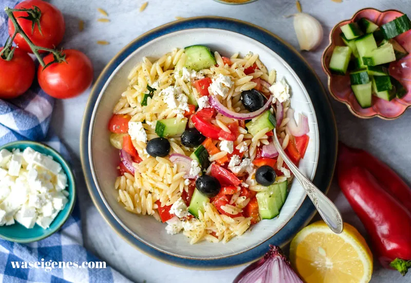 Ein farbenfroher griechischer Kritharaki-Salat in einer großen Glasschale, perfekt für eine Sommerparty.