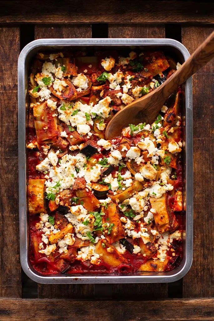 Ein farbenfroher Ratatouille-Maultaschen-Auflauf mit viel Gemüse und Feta, appetitlich angerichtet in einer Auflaufform auf einem rustikalen Holztisch.