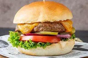 Ein fertig belegter Hamburger, appetitlich angerichtet mit Rindfleisch, geschmolzenem Käse, frischem Gemüse und Sauce.