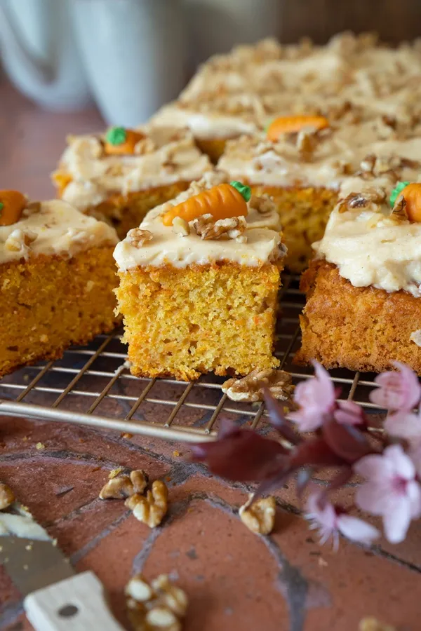 Ein fertig gebackener Rüblikuchen vom Blech, großzügig mit cremiger Frischkäseglasur bestrichen und bereit zum Servieren.