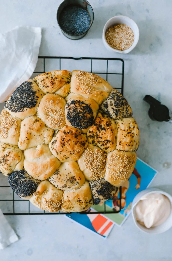 Ein fertiger Brötchenkranz, auf einem Teller angerichtet, mit einem kleinen Schälchen Dip daneben, bereit zum Servieren.