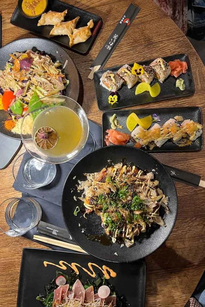Ein Festmahl verschiedener asiatischer Gerichte auf einem Holztisch bei Silk Restaurant in Zagreb, darunter Sushi, Gyoza, Nudeln und Sashimi, bereit für ein genussvolles Essen.