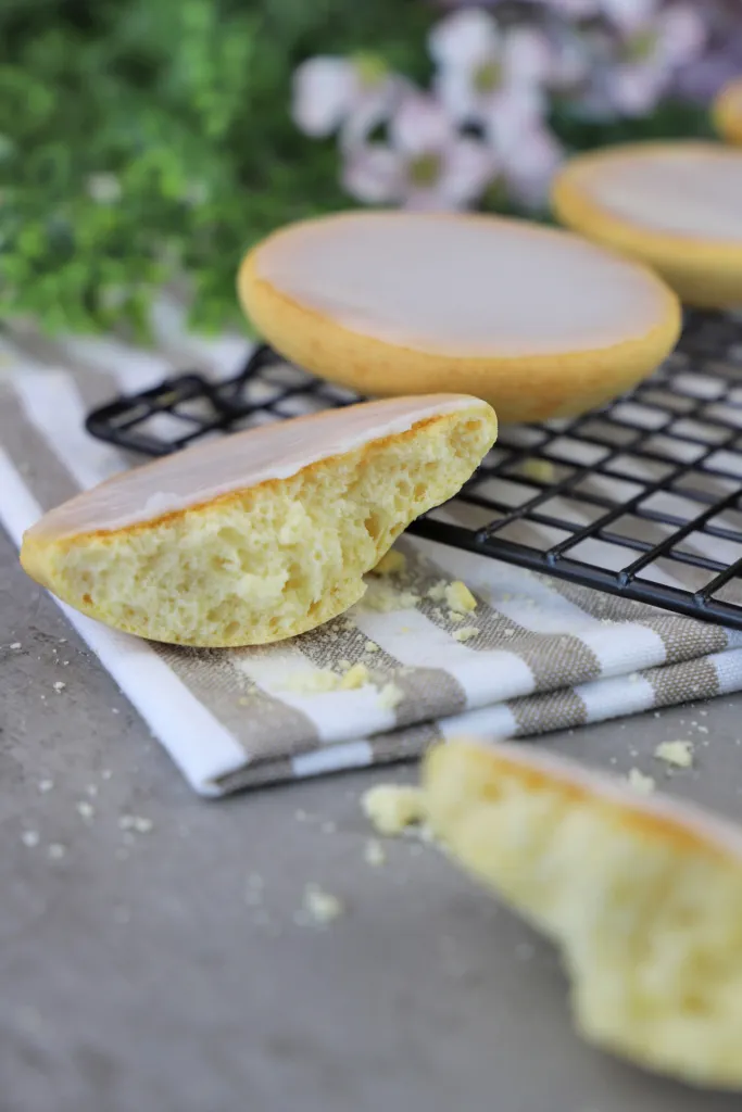 Ein frisch gebackener, runder Amerikaner mit glänzendem, weißem Zuckerguss auf einem Backpapier, bereit zum Anbeißen. Eine klassische Süßigkeit, perfekt zum selber Backen.