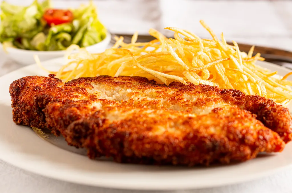 Ein frisch gebratenes Hähnchenschnitzel, perfekt paniert und goldbraun, bereit zum Servieren mit einer Zitronenspalte