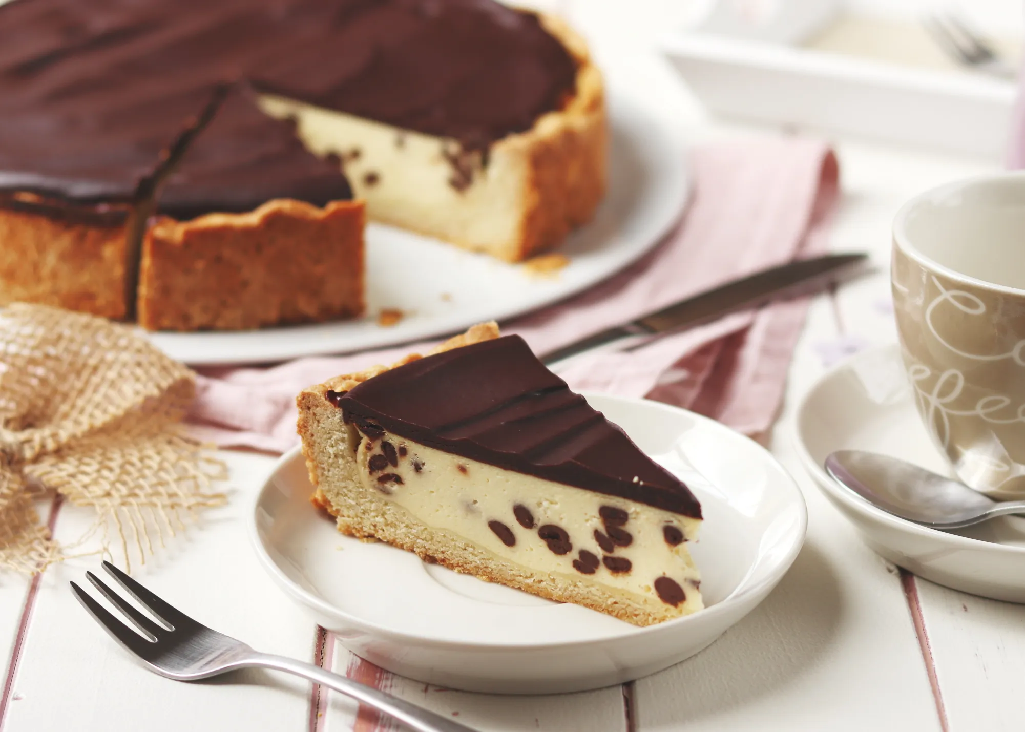 Ein ganzer Käsekuchen mit Schokoglasur auf einer Tortenplatte, mit mehreren bereits entnommenen Stücken.