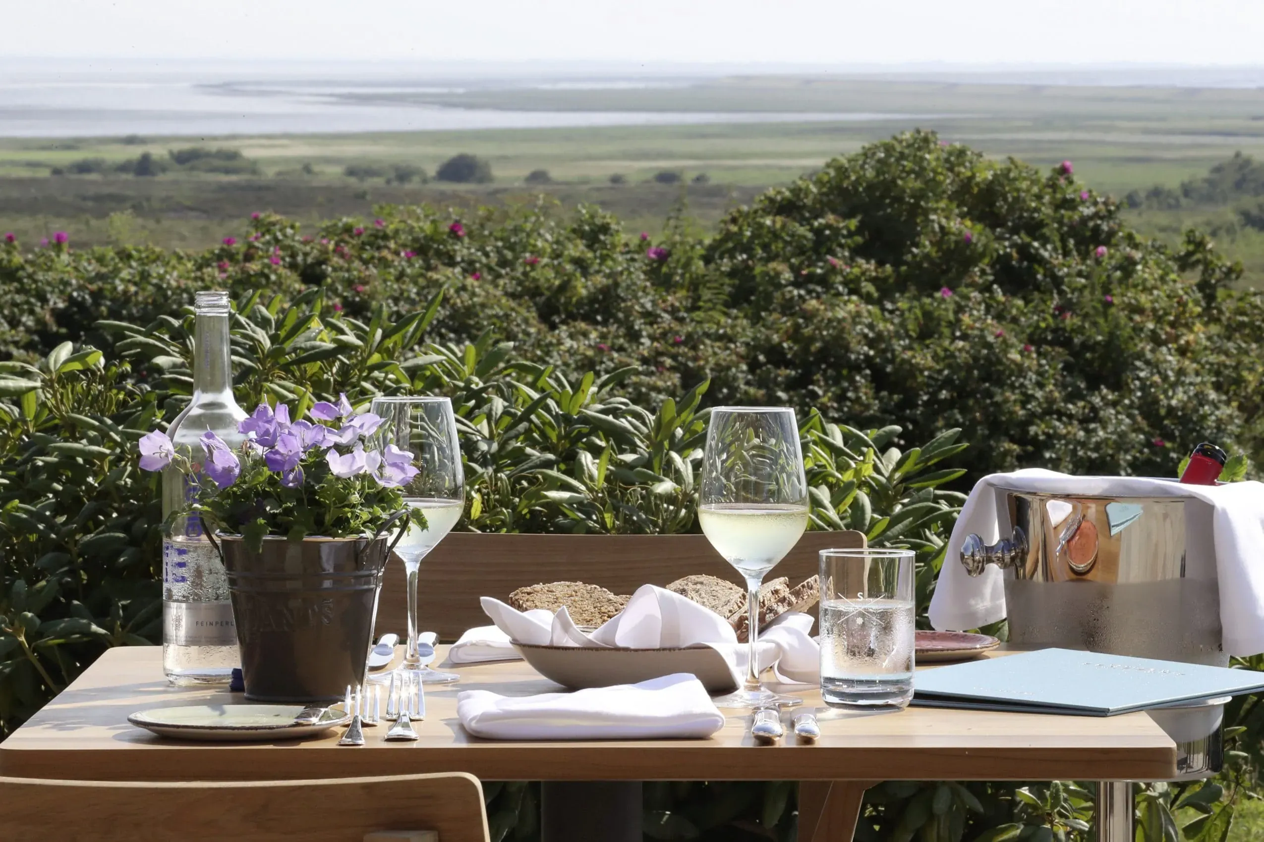 Ein gedeckter Tisch auf der Terrasse des Landhaus Severin's Morsum Kliff mit Blick auf die Dünen und das Wattenmeer, wo gut erzogene Hunde willkommen sind.