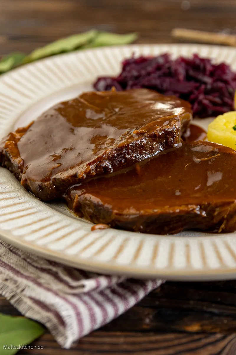 Ein geschnittener, zarter Rinderbraten, dessen Scheiben von dunkler Soße umhüllt sind.