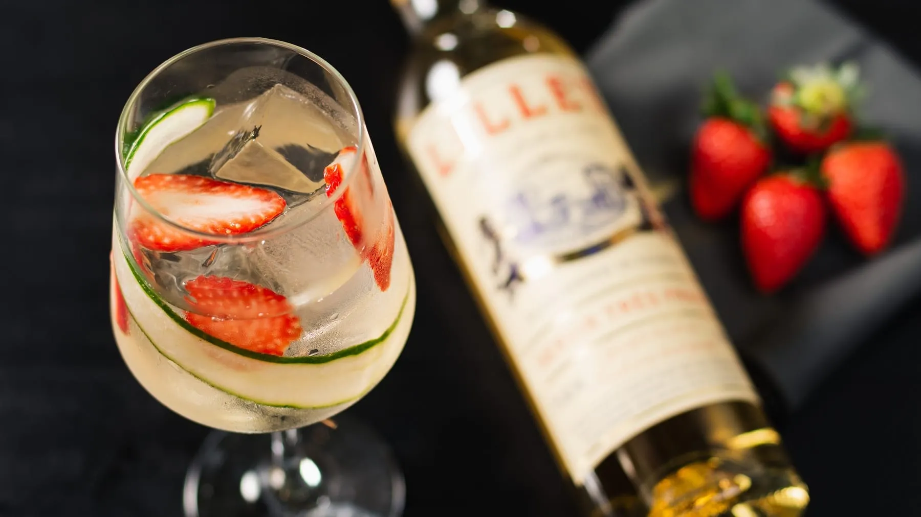 Ein Glas Lillet Vive mit Erdbeeren auf schwarzem Hintergrund