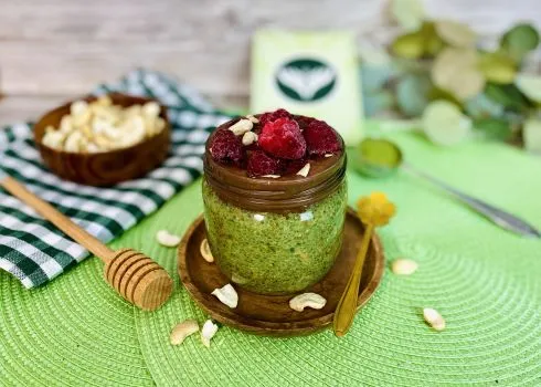 Ein Glas Matcha-Chia-Pudding mit frischen Himbeeren, Schokosauce und Cashewkernen