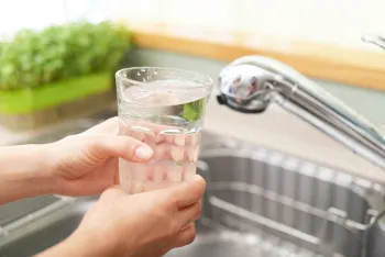 Ein Glas mit frischem Leitungswasser steht auf einem Tisch, im Hintergrund verschwommen eine Küche