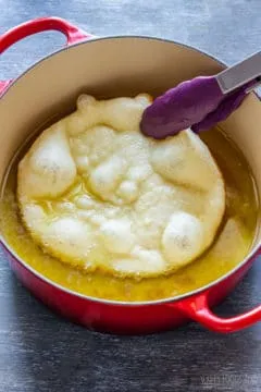 Ein goldbrauner Langos wird aus dem heißen Öl genommen