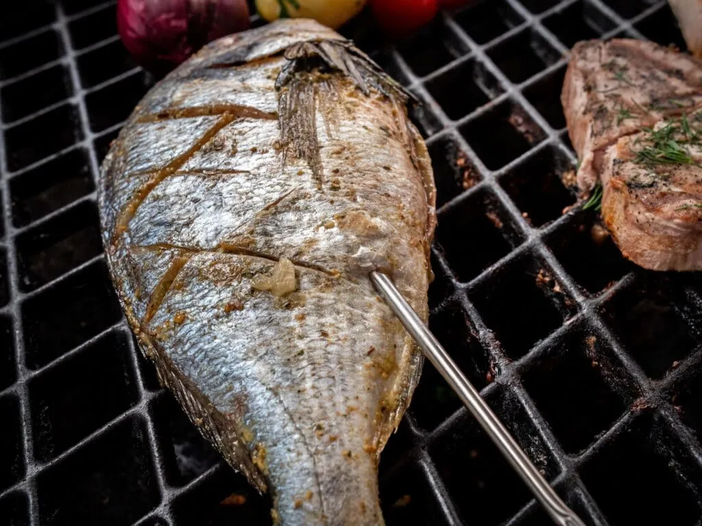 Ein Grillthermometer misst die Kerntemperatur eines Fisches auf dem Grillrost, um den perfekten Garpunkt zu bestimmen.