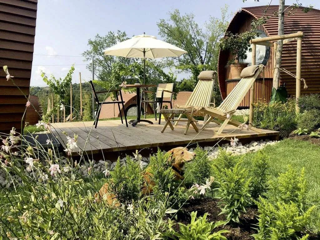 Ein Hund ruht auf der grünen Wiese vor der gemütlichen Terrasse eines Tiny House im Glamping Resort Bliesgau, einem hundefreundlichen Hotel mit Komfort.