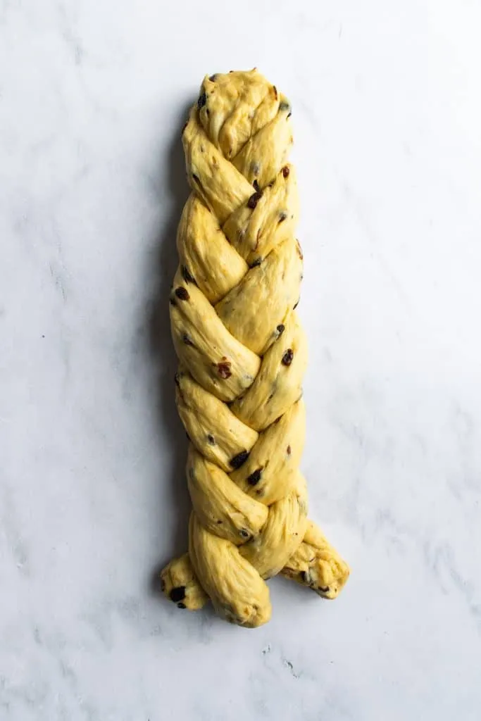 Ein kunstvoll geflochtener Hefezopf auf einer Marmoroberfläche, die Basis für den Osterkranz, noch ungebacken.