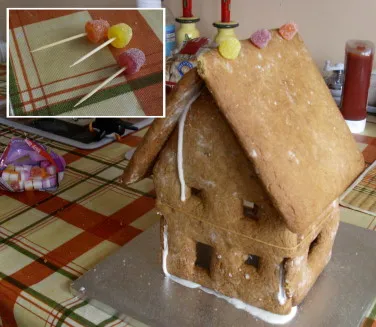 Ein Lebkuchenhaus im Rohbau, die Wände mit Zuckerguss zusammengeklebt und mit Gummibändern fixiert, während der Zuckerguss trocknet.